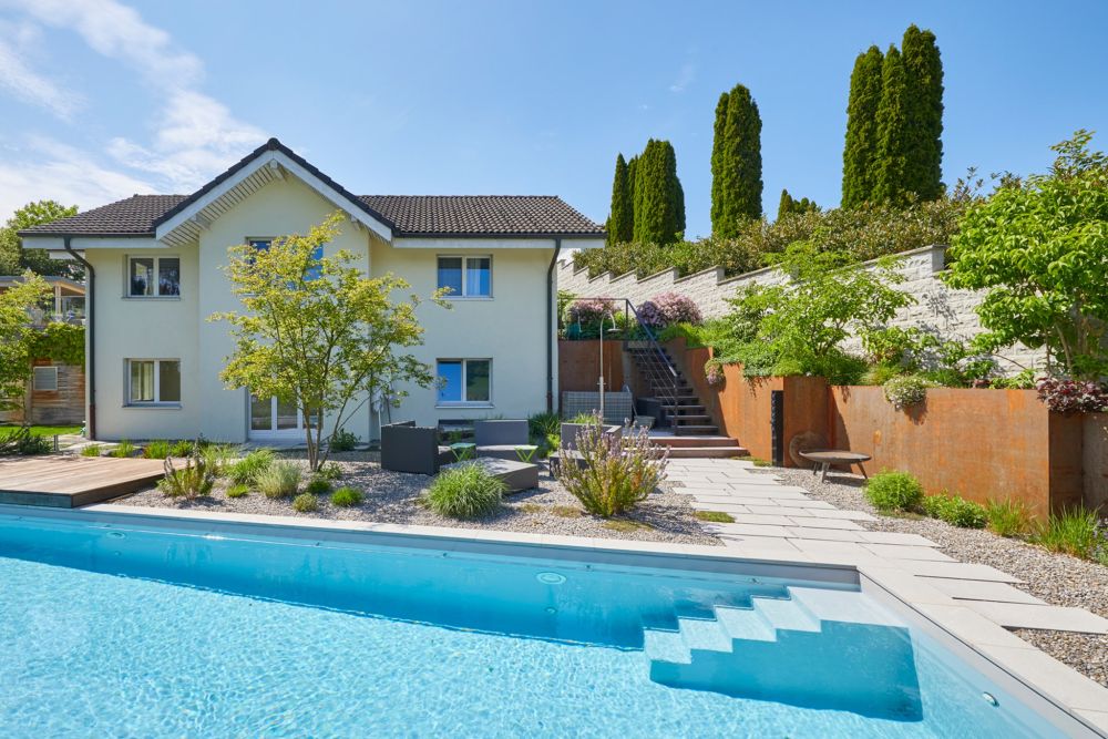 Einfamilienhaus mit Pool und moderner Gartenanlage, Sitzplatz mit Sträucher, bepflanzte Hochbeete aus Metall in Rostoptik