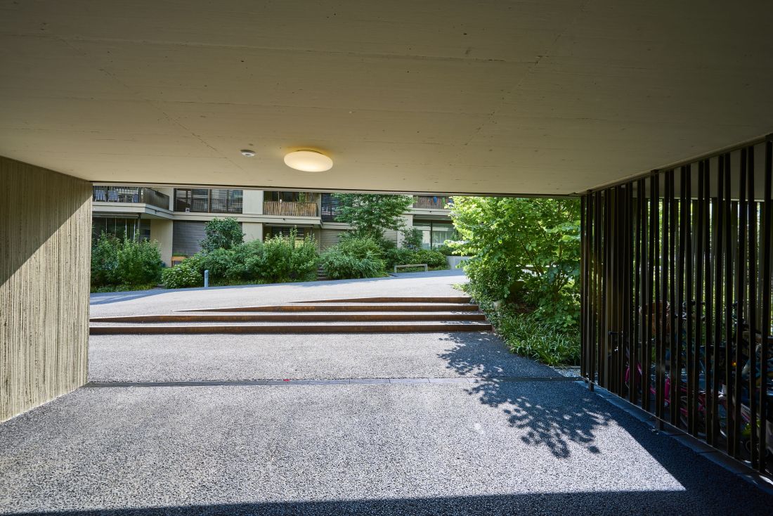 Blick durch eine Unterführung einer Wohnsiedlung auf eine moderne, asymmetrische Treppe aus Stahl in Rostoptik