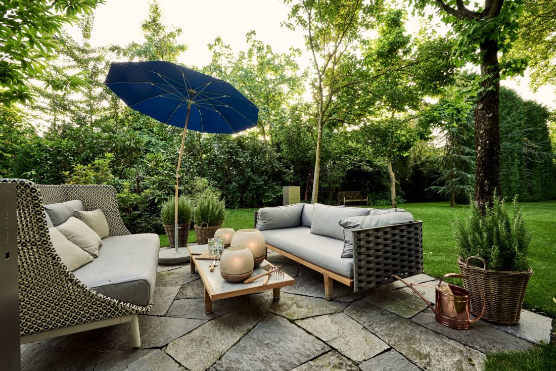 Moderne Gartensitzgruppe mit Polstersofa, blauem Sonnenschirm und Pflanzen auf Natursteinplatte, Gartenbau Aargau