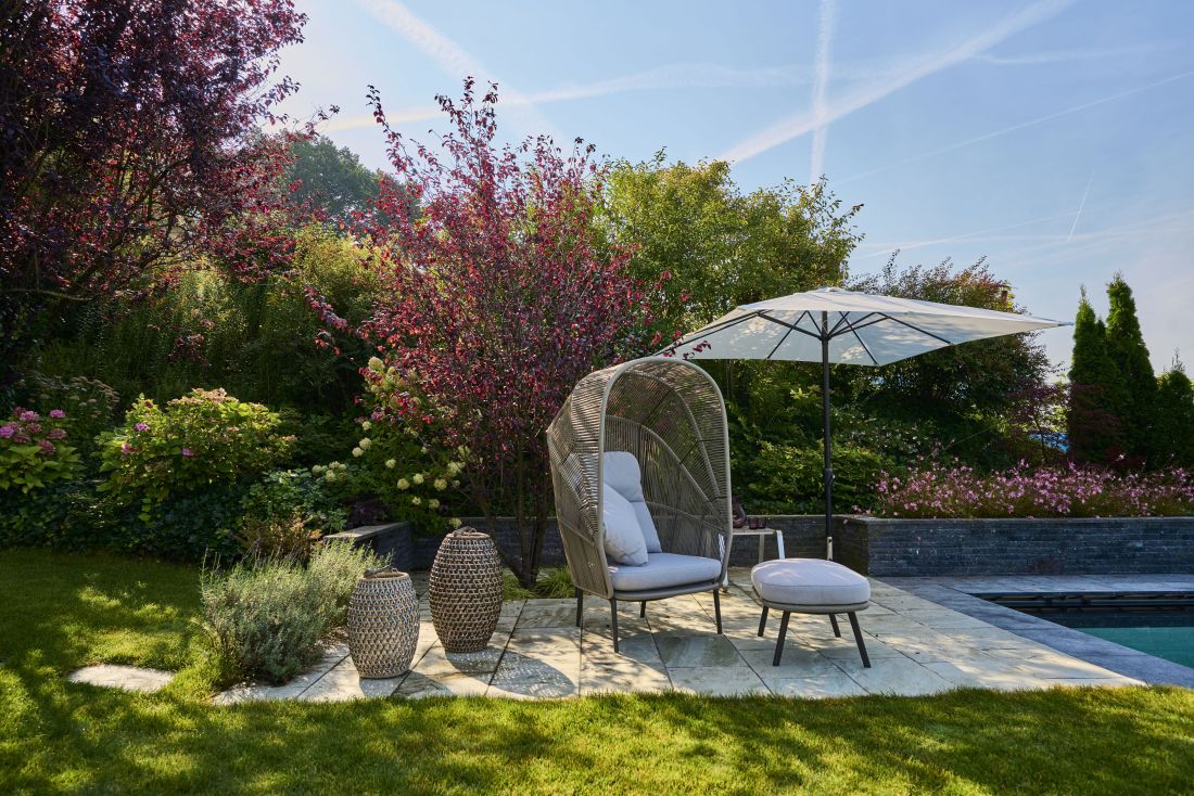 Moderner Sitzplatz mit Korbsessel, Sonnenschirm und Gartenpflanzen im Gartenbau Aargau von Schoop Gartenbau