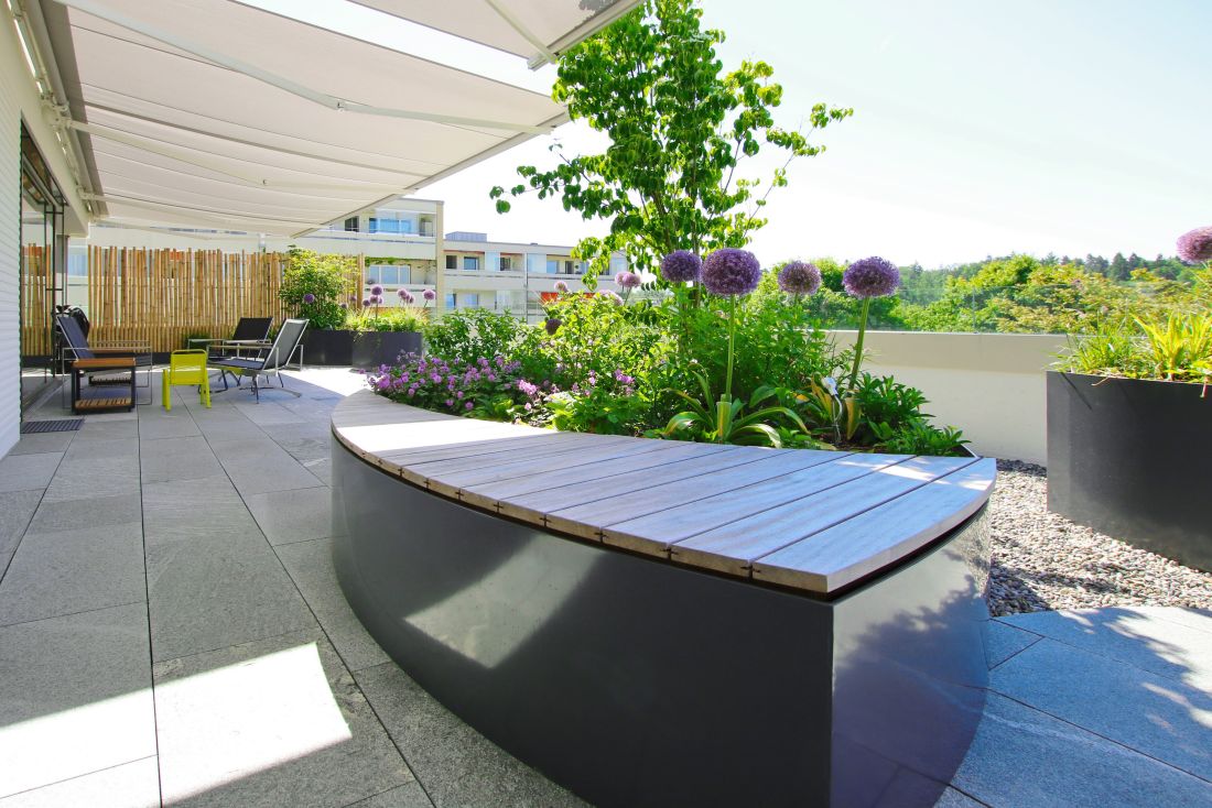 Moderne Dachterrasse im Aargau mit Sitzbank, Pflanzbeeten, Sonnenschutz und Sitzmöbeln auf Flachdach mit Steinplatten