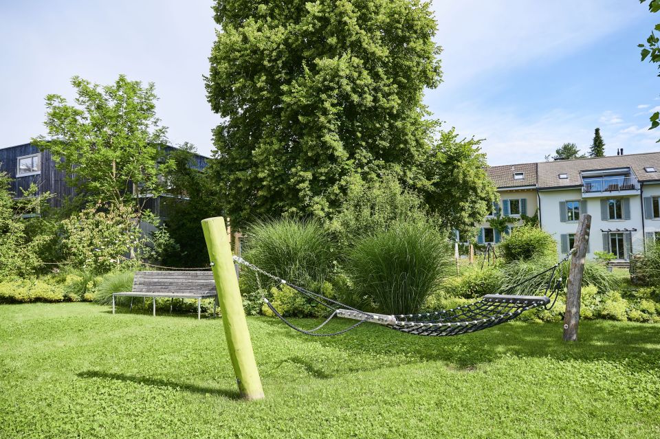 Hängematte über Rasen, Bäume und Sträucher im Hintergrund mit Holzbank, Gartenbau Schoop Aargau