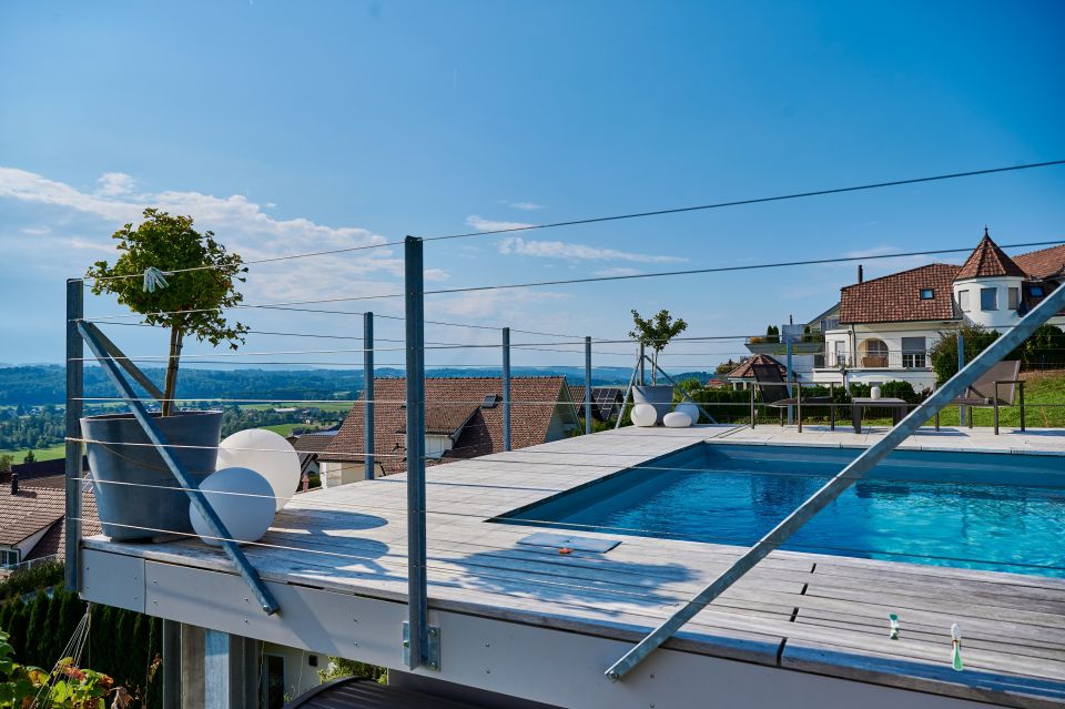 Pool auf einer Terrasse mit grosszügigem Ausblick, blauem Himmel und im Hintergrund ein Haus mit kleinem Turm