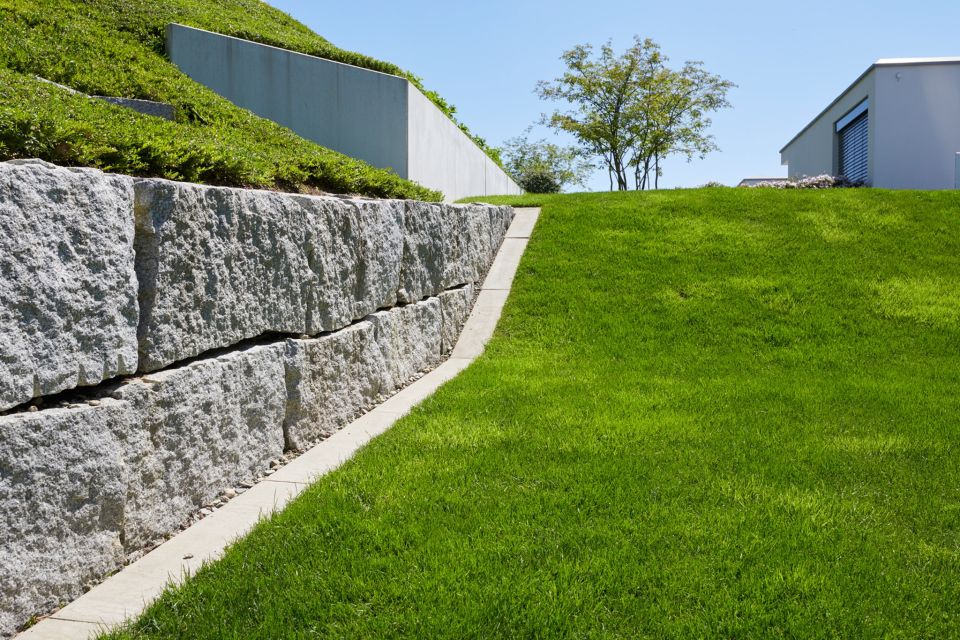 Gepflegter Garten mit grünem Rasen und Steinmauer als Beispiel für Gartenpflege Aargau von Schoop Gartenbau