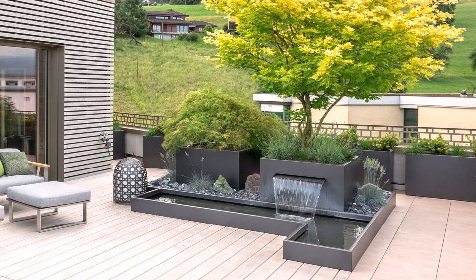 Moderne Terrassengestaltung mit Brunnen, Hochbeet, Pflanzen und Plattenbelag  von Schoop Gartenbau