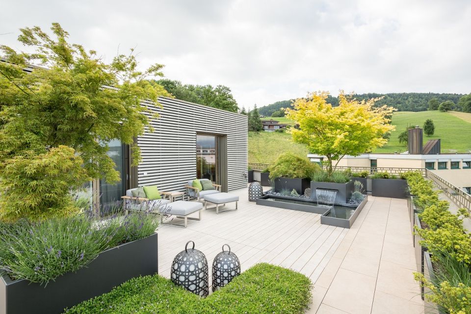 Moderne Dachterrasse mit Holzbelag, Loungemöbeln, Pflanzkübeln und Wasserspiel in ländlicher Umgebung im Aargau, Schweiz