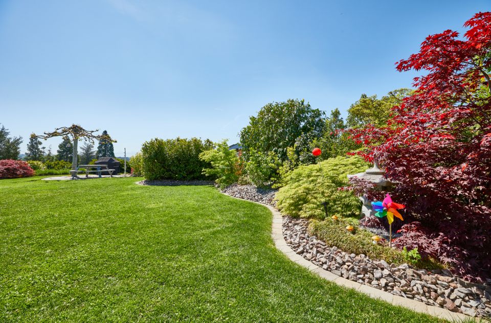 Schöne Gartenanlage mit Rasen und bepflanztem Beet, Sträucher in verschiedenen Farben und einem bunten kleinen Windrad