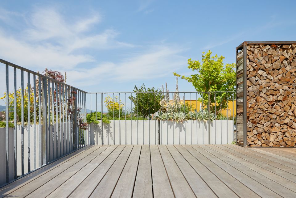 Dachterrasse mit Holzbelag, Metallgeländer, Pflanzen und Holzstapel als Sichtschutz im Aargau, Schweiz
