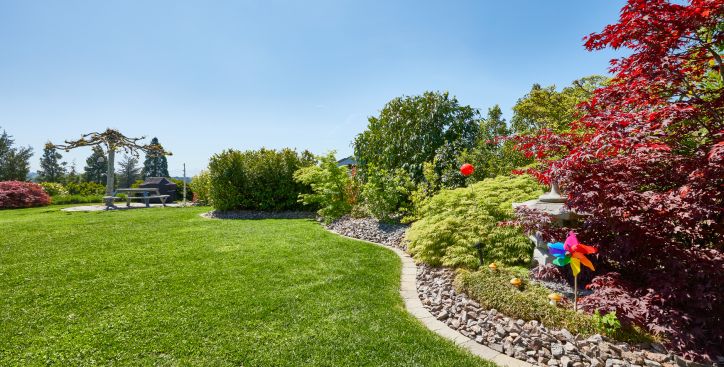 Schöne Gartenanlage mit Rasen und bepflanztem Beet, Sträucher in verschiedenen Farben und einem bunten kleinen Windrad